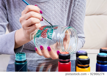 A girl paints a glass jar with stained glass paints 92966274