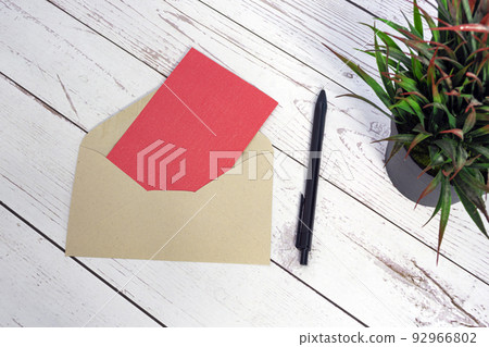 Red card mockup with envelope, pen and potted plant on wooden table. 92966802