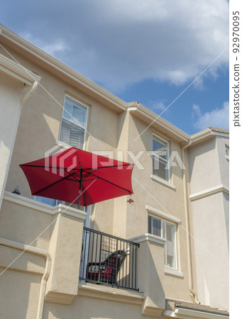 Vertical White puffy clouds Red umbrella on a balcony of a townhouse with cream wall exterio 92970095