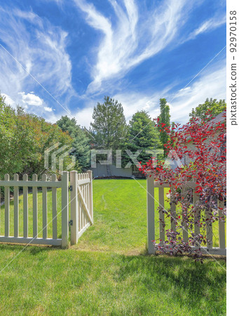 Vertical Whispy white clouds Backyard with picket fence and gate on a green lawn Vertical Whispy white clouds Backyard with picket fence and gate on a green lawn 92970158