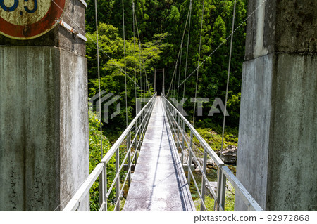 An old, thin suspension bridge over a river deep in the mountains 92972868