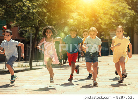 Group of joyful children running down the summer street Group of joyful children running down the summer street 92973523