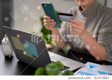Close up shot of females hands holding credit card typing message on smart phone with technology icons for shopping online. 92974663