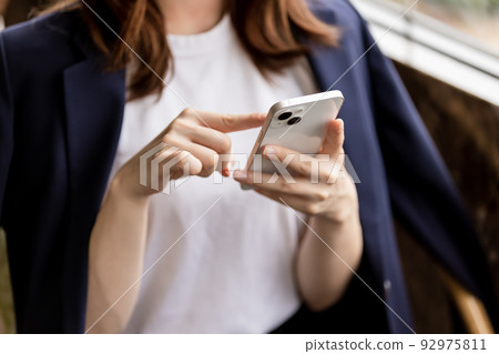 A woman operating a smartphone, in hand, faceless A woman operating a smartphone, in hand, faceless 92975811