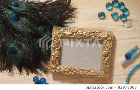 Blue Jewelry and Peacock Feathers With Gold Picture Frame on Wooden Table 92978068