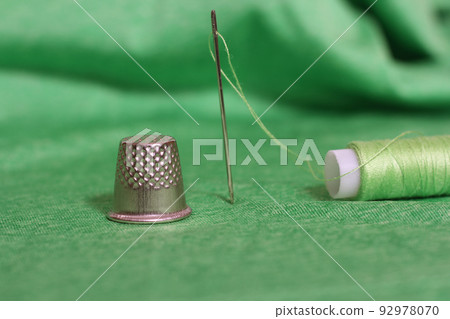Spool of Green Thread, Thimble and Needle on Green Fabric 92978070