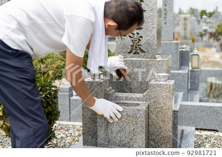 Senior man visiting a grave and cleaning the grave 92981721