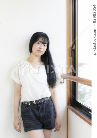 Young woman in a miniskirt standing by the window Young woman in a miniskirt standing by the window 92982054