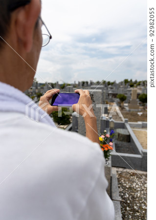 A senior man visiting a grave and taking a picture of the grave with a smartphone after cleaning A senior man visiting a grave and taking a picture of the grave with a smartphone after cleaning 92982055