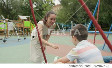 4K. Mom rides her son on a swing in the park in the summer 4K. Mom rides her son on a swing in the park in the summer 92982528