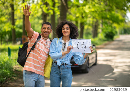 Dark-skinned couple hitchhiking on the road in the countryside Dark-skinned couple hitchhiking on the road in the countryside 92983089