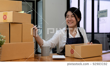 Smiling entrepreneur checking order on delivery box on work desk at home 92983192