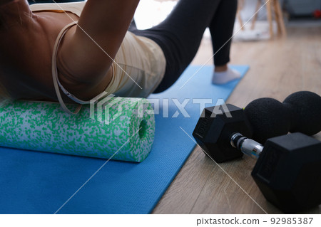 Closeup of woman riding cork massage roller to relieve tension in back muscles Closeup of woman riding cork massage roller to relieve tension in back muscles 92985387