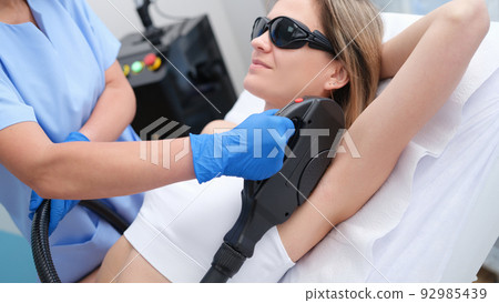 Woman undergoes hair removal procedure with photoepilator or laser hair removal of armpits in salon 92985439