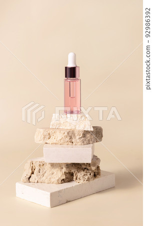 Pink glass cosmetic dropper bottle on beige travertine stones on light yellow close up Pink glass cosmetic dropper bottle on beige travertine stones on light yellow close up 92986392