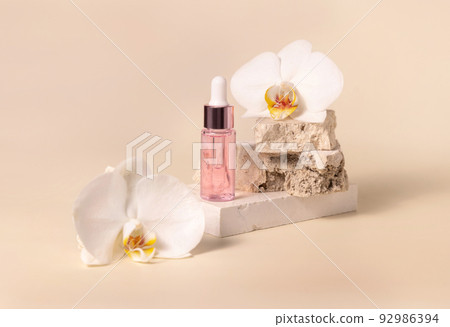 Dropper Bottle on stone near white orchid flowers on light yellow close up Dropper Bottle on stone near white orchid flowers on light yellow close up 92986394