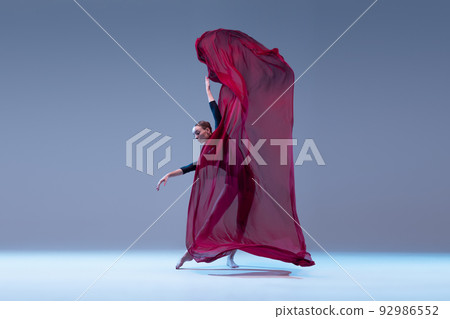 Portrait of young ballerina dancing covered in deep red transparent fabric isolated over blue grey studio background. Graceful tender Portrait of young ballerina dancing covered in deep red transparent fabric isolated over blue grey studio background. Graceful tender 92986552