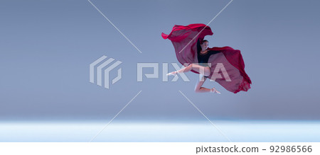 Portrait of young ballerina dancing with deep red fabric isolated over blue grey studio background. Flying like a butterfly 92986566