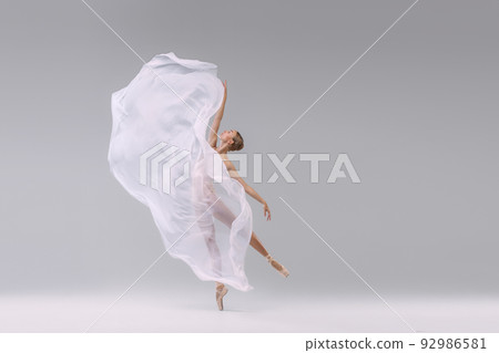 Portrait of young ballerina dancing with fabric isolated over grey studio background. Standing on tiptoe. Weightless transparent cloth 92986581