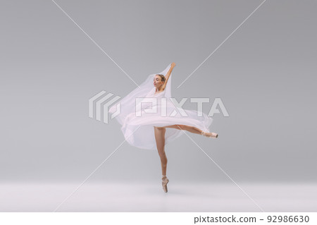 Portrait of young flexible ballerina dancing with transparent fabric isolated over grey studio background. Tenderness, grace 92986630
