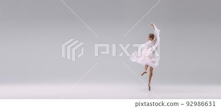 Portrait of young ballerina dancing covered with white transparent fabric isolated over grey studio background. Classic movements Portrait of young ballerina dancing covered with white transparent fabric isolated over grey studio background. Classic movements 92986631