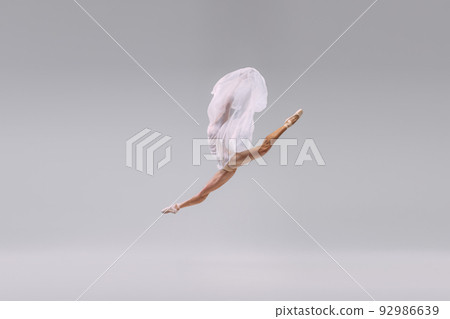 Portrait of young ballerina dancing, jumping in a twine with transparent fabric isolated over grey studio background Portrait of young ballerina dancing, jumping in a twine with transparent fabric isolated over grey studio background 92986639