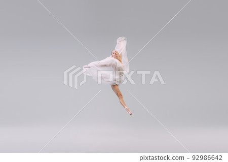 Portrait of young ballerina dancing, jumping with transparent fabric isolated over grey studio background. Leap 92986642