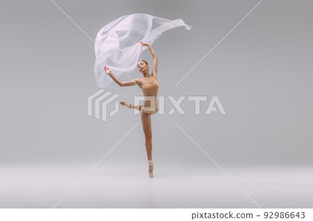 Portrait of young beautiful ballerina dancing with transparent fabric isolated over grey studio background. Grace Portrait of young beautiful ballerina dancing with transparent fabric isolated over grey studio background. Grace 92986643