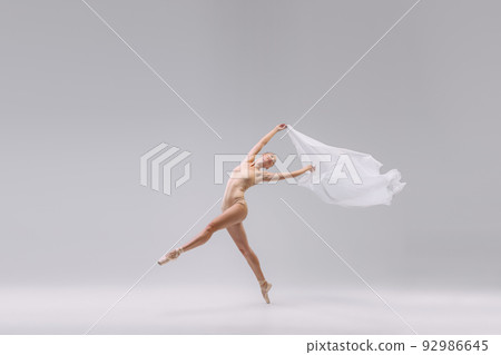 Portrait of young tender ballerina dancing with fabric isolated over grey studio background. Theatrical performance 92986645
