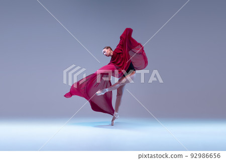Portrait of young ballerina dancing with deep red transparent fabric isolated over blue grey studio background. Grace Portrait of young ballerina dancing with deep red transparent fabric isolated over blue grey studio background. Grace 92986656