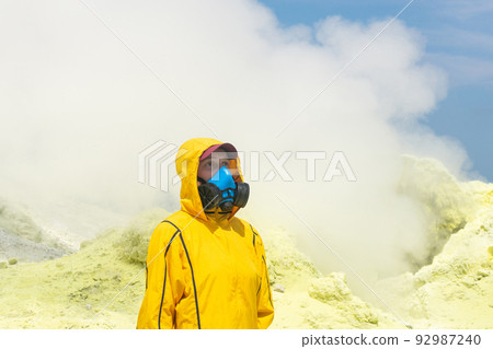 female volcanologist in a respirator against the background of a smoking fumarole on the slope of a volcano 92987240