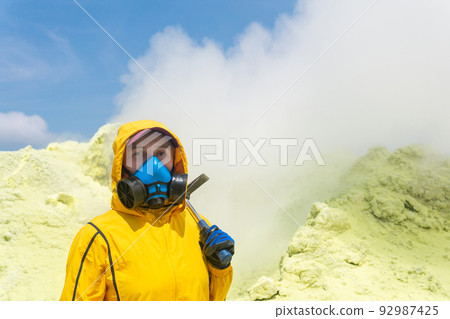 female volcanologist with a geological hammer and in a respirator against the backdrop of a smoking fumarole on the slope of a volcano female volcanologist with a geological hammer and in a respirator against the backdrop of a smoking fumarole on the slope of a volcano 92987425