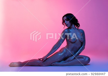 Sensual naked woman with body art sitting in neon studio 92988447