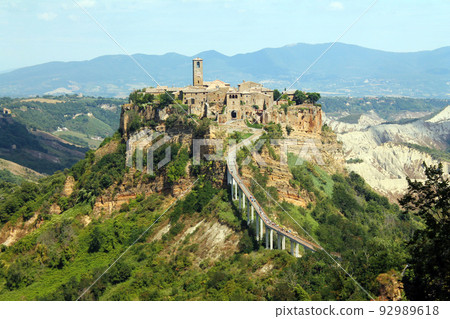 Close op of the historical civita village of Bagnoregio standing on a cliff with the long pedestrian bridge 92989618