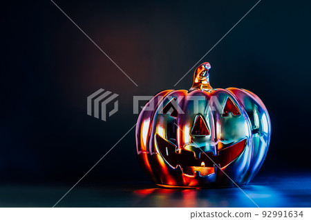 Neon spooky halloween pumpkin, Jack O Lantern, with an evil face and eyes made with holographic glass on dark background with copy space. Festive Halloween decor concept 92991634
