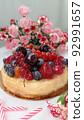 Berry birthday cake. Cheesecake with cherries, raspberries, currants and blueberries. Cake, pink candles and red flowers on a white background. Photo for stories. 92991657