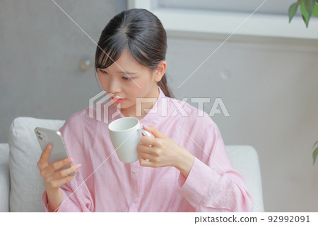 A woman holding a coffee cup and looking at a smartphone with a strange expression 1 A woman holding a coffee cup and looking at a smartphone with a strange expression 1 92992091
