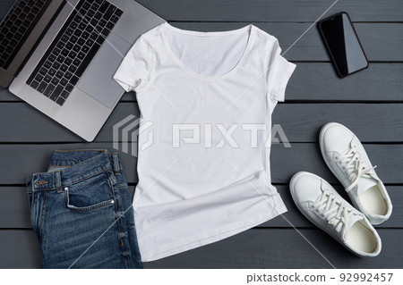 Flat lay of white t-shirt lying on rough wooden planks with laptop, smartphone and apparel accessories. Flat lay of white t-shirt lying on rough wooden planks with laptop, smartphone and apparel accessories. 92992457