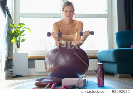 Emotional portrait of beautiful attractive fitness woman on ball with dumbbells Emotional portrait of beautiful attractive fitness woman on ball with dumbbells 92992633