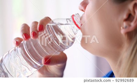 Closeup of young woman drinking water from plastic bottle Closeup of young woman drinking water from plastic bottle 92992689