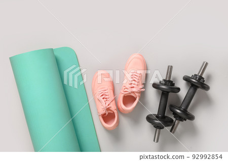 Sport and fitness equipment, female pink shoes, yoga mat on grey background. Sport and fitness equipment, female pink shoes, yoga mat on grey background. 92992854