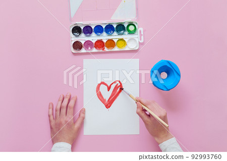 child draws a card for Mother's Day, uses a brush and watercolor 92993760