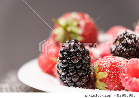 Raspberries, strawberries and blackberries sprinkled with sugar, close-up. 92993993