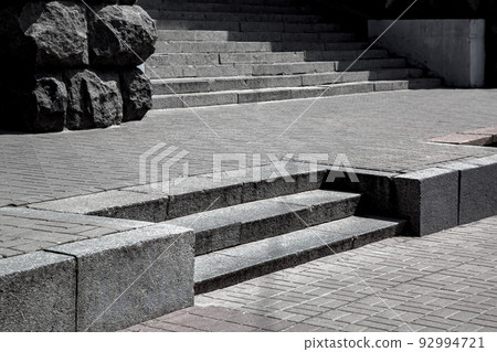 Gray granite steps in the middle of stone tile street pavement brick pattern, cityscape with walkway near building and stairs in sunny day, floor view, nobody. Gray granite steps in the middle of stone tile street pavement brick pattern, cityscape with walkway near building and stairs in sunny day, floor view, nobody. 92994721