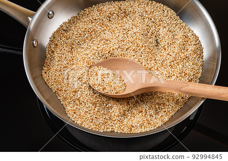 Sesame seeds toasting in a stainless steel frying pan. Roasting white til in a skillet. 92994845