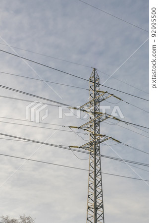 Electric pole metal truss with wires against a cloudy sky. 92995500