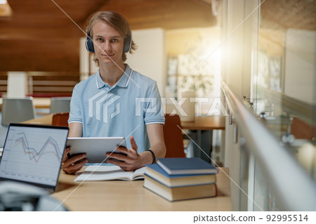 Smiling Male student sits in headphones in library and studies using a digital tablet 92995514