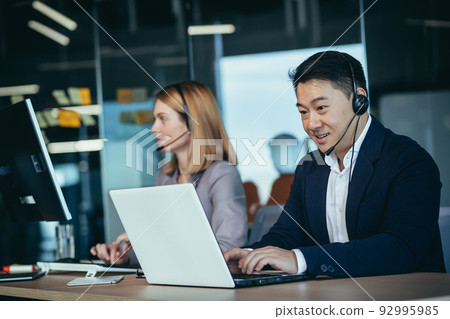 Happy call center employee communicates with customers, advises on video call, remotely, asian business man Happy call center employee communicates with customers, advises on video call, remotely, asian business man 92995985