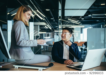Female boss flirts with male employee, businesswoman sitting at desk and smiling then Asian 92996033