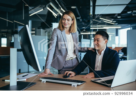 Female boss flirts with male employee, businesswoman sitting at desk and smiling then Asian 92996034